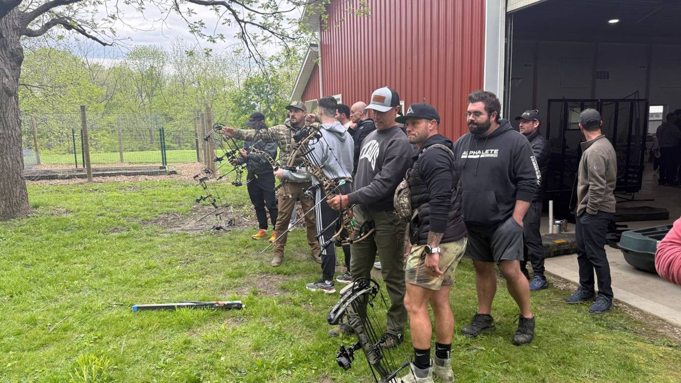 Men shooting compound bows by the red barn